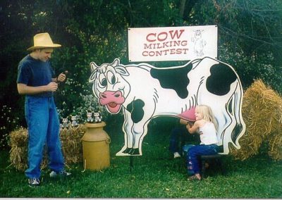 picture of girl participating in a cow milking contest with a cutout and fake cow