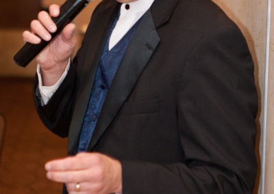 DJ holding microphone and wearing a tux and hat